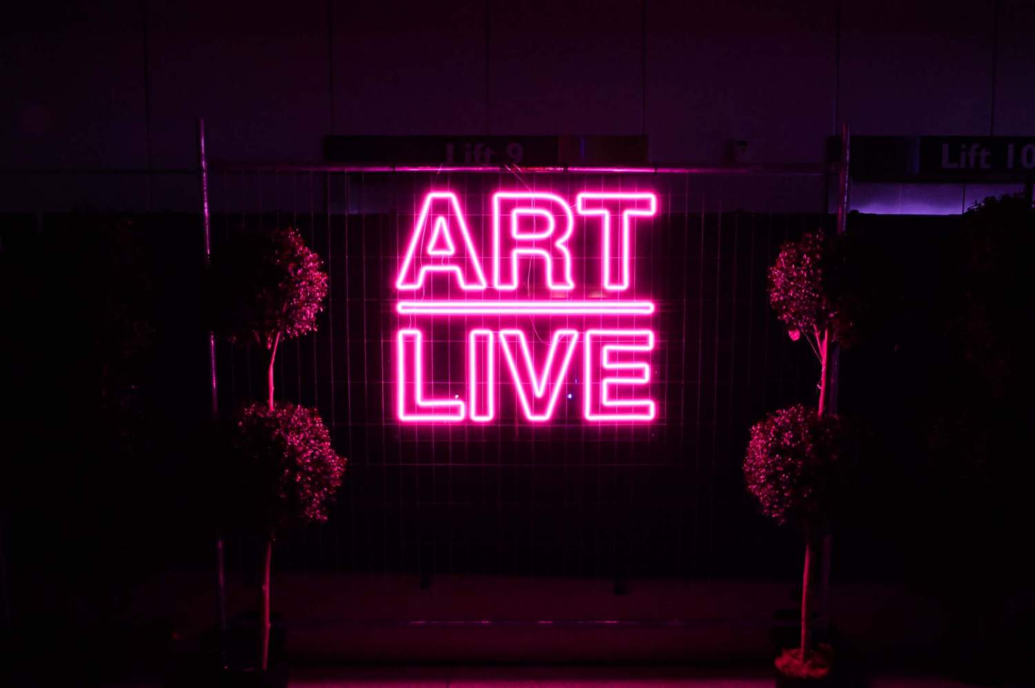 Pink neon light text sign "Art Live" in the park, close-up